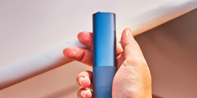 A woman holding an IQOS device looking at a laptop.